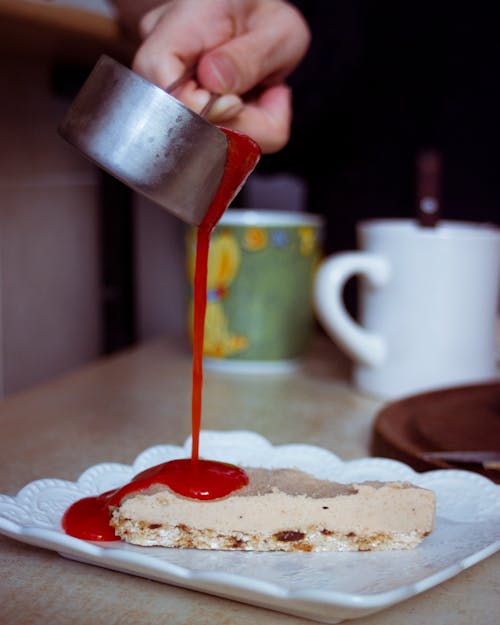 A Person Pouring a Red Syrup on a Pastry