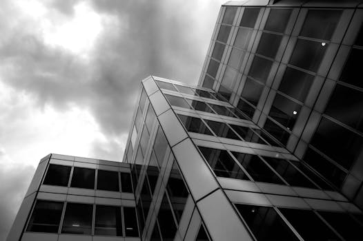 在戏剧性多云天空下，现代玻璃摩天大楼的低角度单色视图