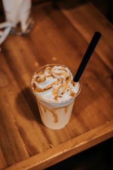 A tempting vertical shot of a caramel iced coffee topped with whipped cream and a straw.