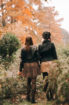两名穿着皮夹克的女子走过一片秋叶环绕、充满活力的森林