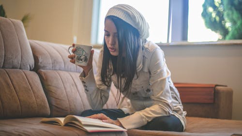 Young Girl Sitting on Brown Couch Reading a Book