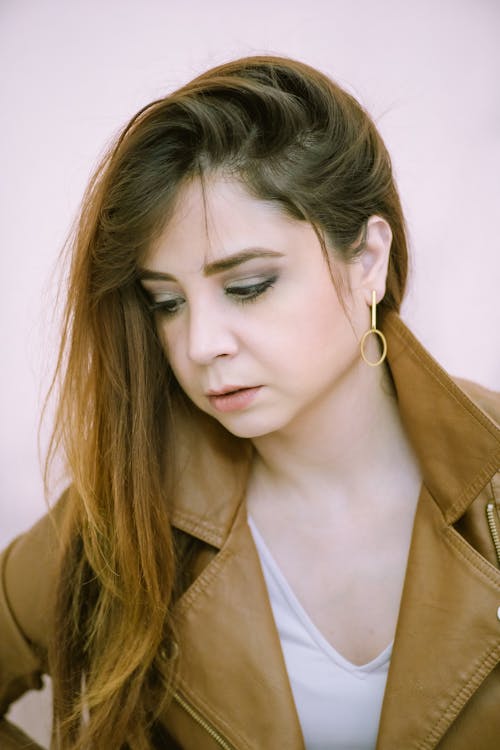 Headshot of young attractive female in casual outfit with long hair and makeup looking down against light background