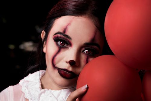 Free Close-up portrait of a woman in creepy clown makeup holding red balloons, perfect for Halloween themes. Stock Photo