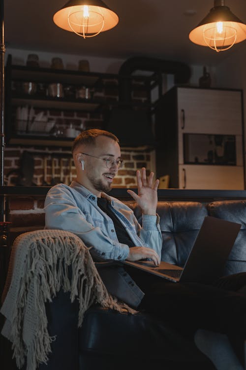 Free Bearded Man Wearing Denim Jacket Sitting on Couch Using his Laptop  Stock Photo