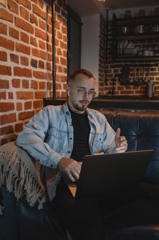 Adult man working remotely on a laptop in a cozy urban setting with exposed brick walls.