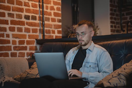 A man in casual attire working on a laptop indoors, symbolizing remote work lifestyle.