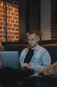 A man works on a laptop from a comfy couch in a stylish home setting.