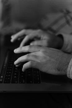 Black and white image of hands typing on a laptop keyboard, highlighting focus and productivity.