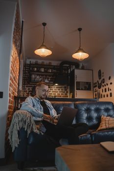 Man working remotely on laptop on a couch in a stylish urban apartment.