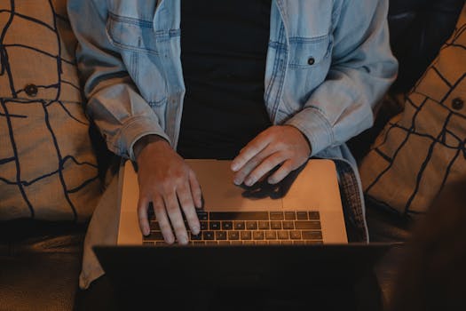A close-up view of a person typing on a laptop, seated comfortably indoors.