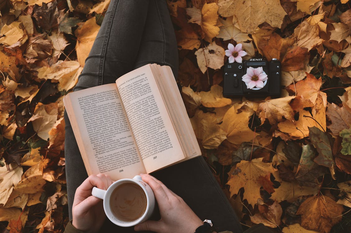 Person Holding a Cup of Coffee while Reading a Book