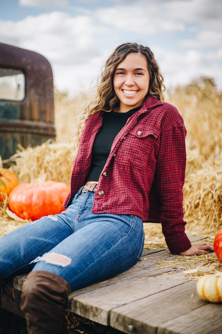 Smiling Woman Sitting On Truck With Hay And Pumpkins