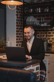 Man working remotely in stylish kitchen, wearing blazer and headphones, using laptop.