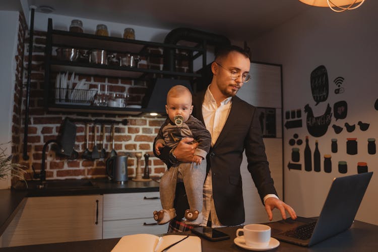 A Man Working From Home While Carrying A Baby