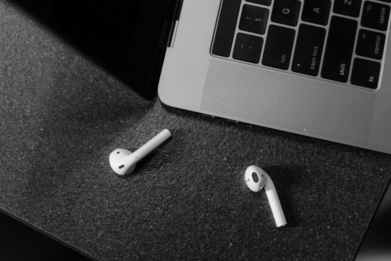 black and white image of wireless earbuds and laptop top view