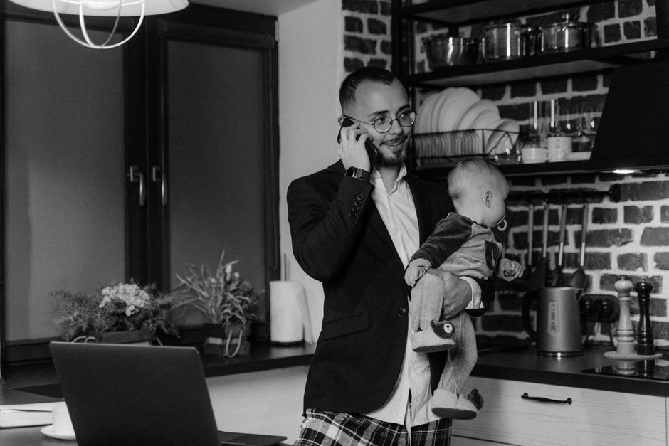 Un père jongle entre son bébé et son téléphone dans une cuisine moderne.