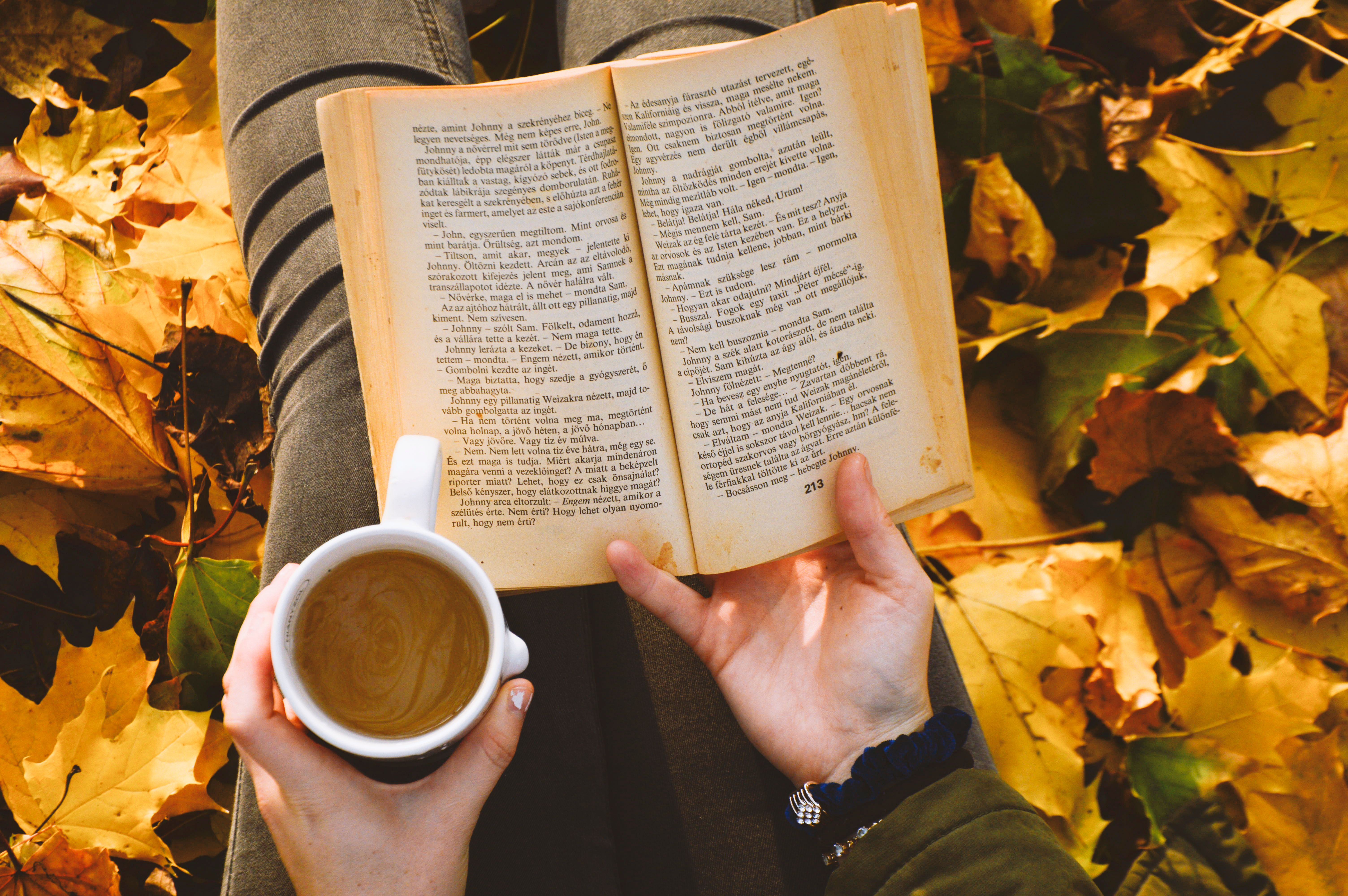 Warm autumn scene of reading a book with coffee among fallen leaves. Perfect for cozy, relaxing themes.