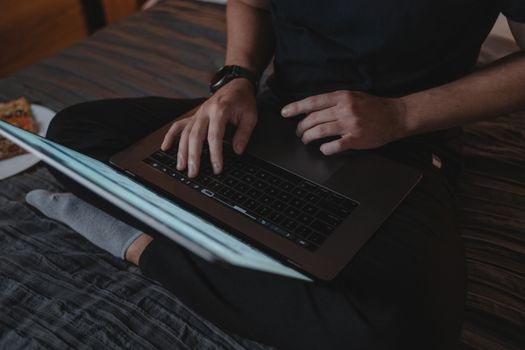 Man sitting cross-legged on bed using laptop, relaxing indoors.