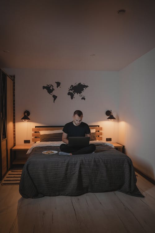 Man in Black Shirt Using a Computer Laptop Sitting on His Bed 
