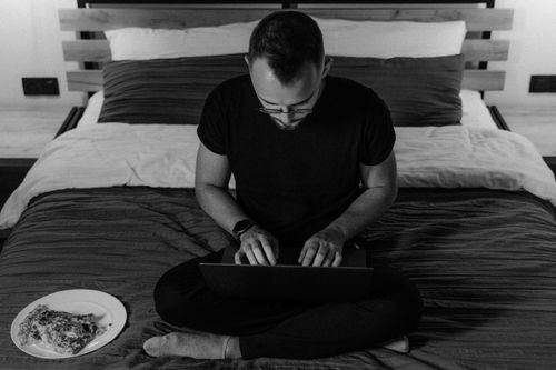 Free Man working on a laptop in a cozy bedroom, embracing remote work lifestyle. Stock Photo