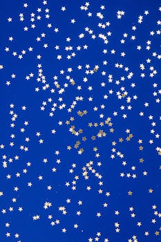Golden star confetti scattered on a deep blue surface, creating a festive and whimsical pattern.
