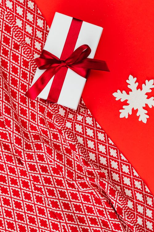 Free A festive Christmas gift wrapped with a red ribbon on a red background with a snowflake decoration. Stock Photo