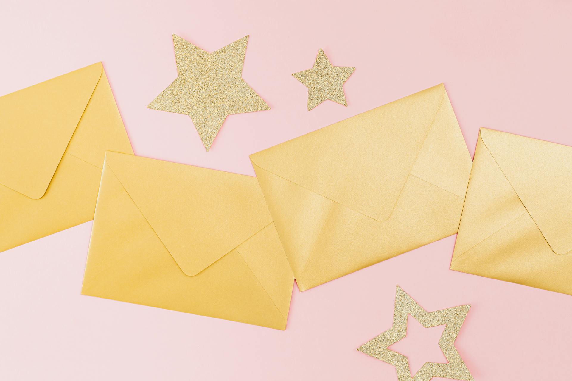 Golden envelopes and glittery stars on a pink background, perfect for festive celebrations.