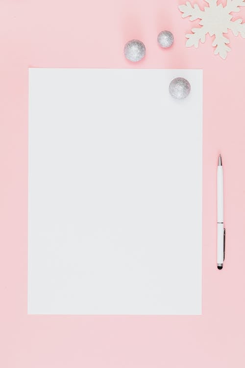 Close-Up Shot of a White Bond Paper and a Pen on a Pink Surface