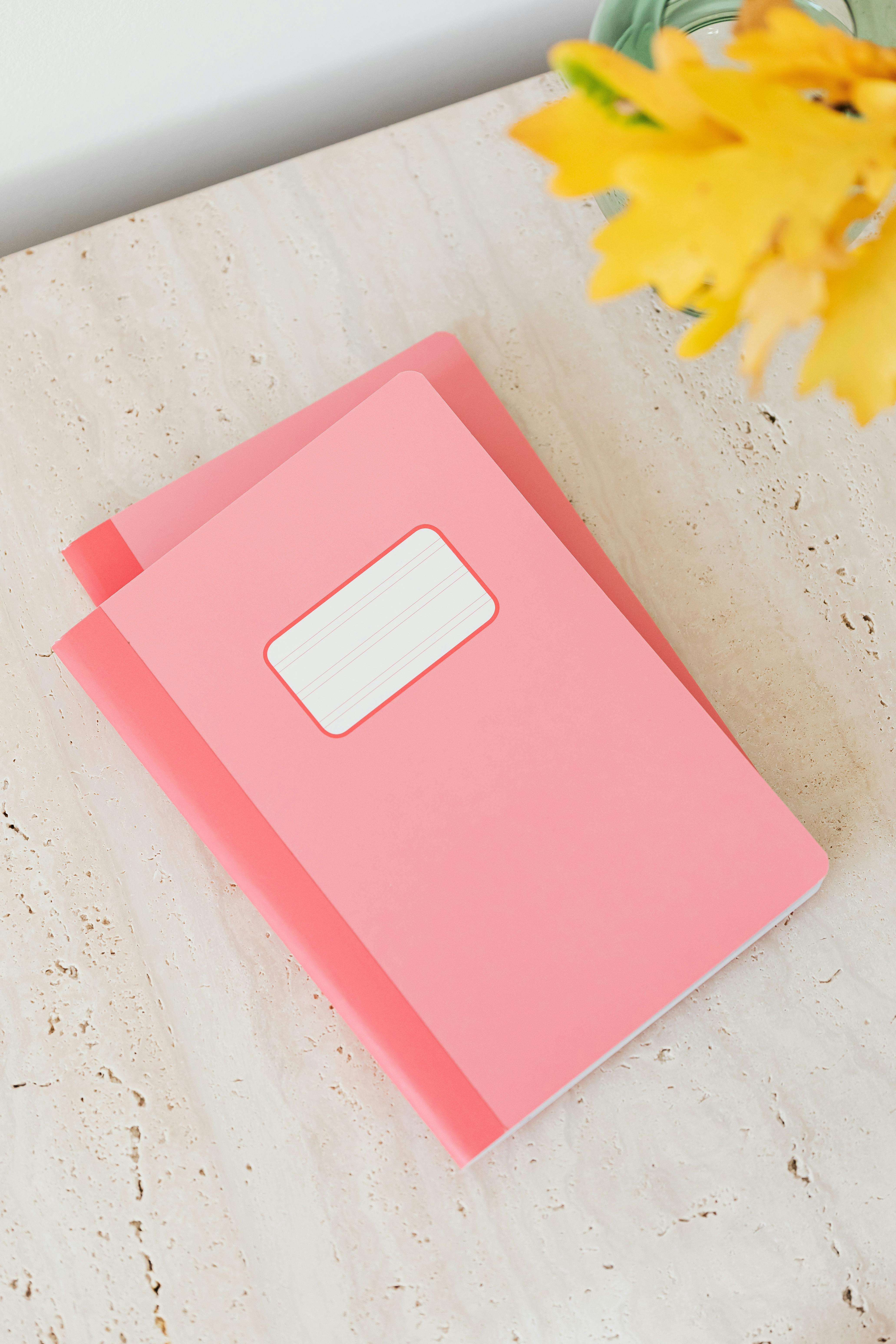 粉色笔记本在大理石上的顶视图，带有黄色花朵，非常适合文具主题项目