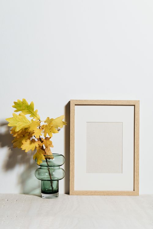 Free Minimalist still life of oak leaves in a vase beside an empty wooden frame. Stock Photo