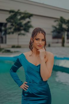 Portrait of a woman in a teal dress posing by a pool with an elegant expression.