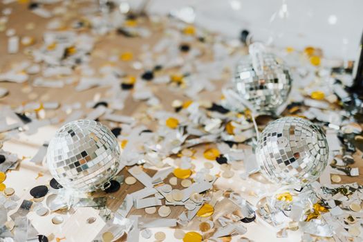 Close-up of disco balls surrounded by colorful confetti on a party table.