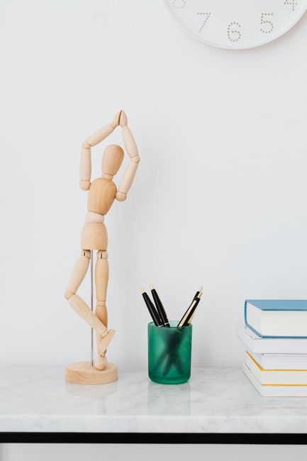 Elegant desk with wooden mannequin, books, and pens in green holder, perfect for a minimalist setup.