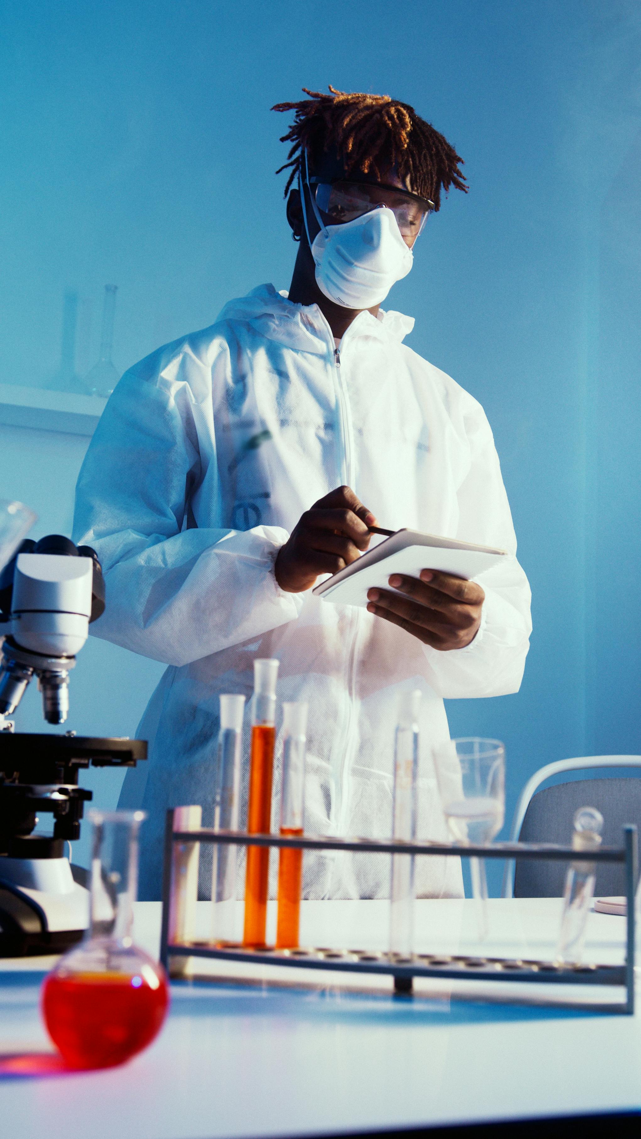 a man wearing face mask and lab coat while standing by the table with his experiments