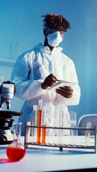 一名科学家穿着防护装备，在实验室里用显微镜检查测试样本