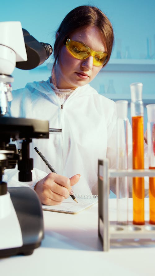 A Woman Writing on Her Notebook While Doing an Experiment