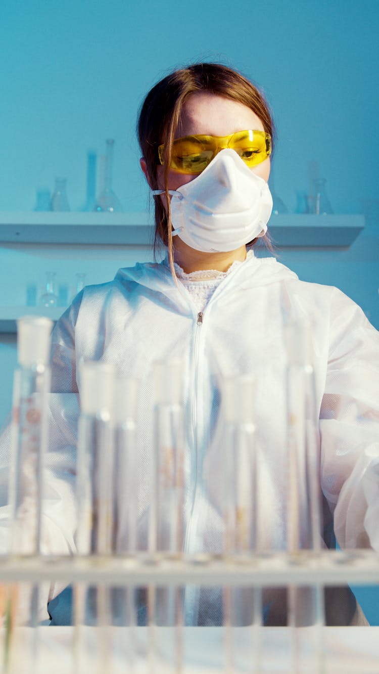 A Woman Wearing A Face Mask And Lab Coat While Doing An Experiment