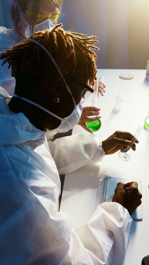 A Man Writing on His Notebook While Doing an Experiment