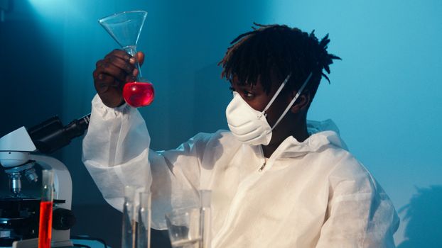 一名科学家穿着防护服，在实验室里检查一种红色化学物质