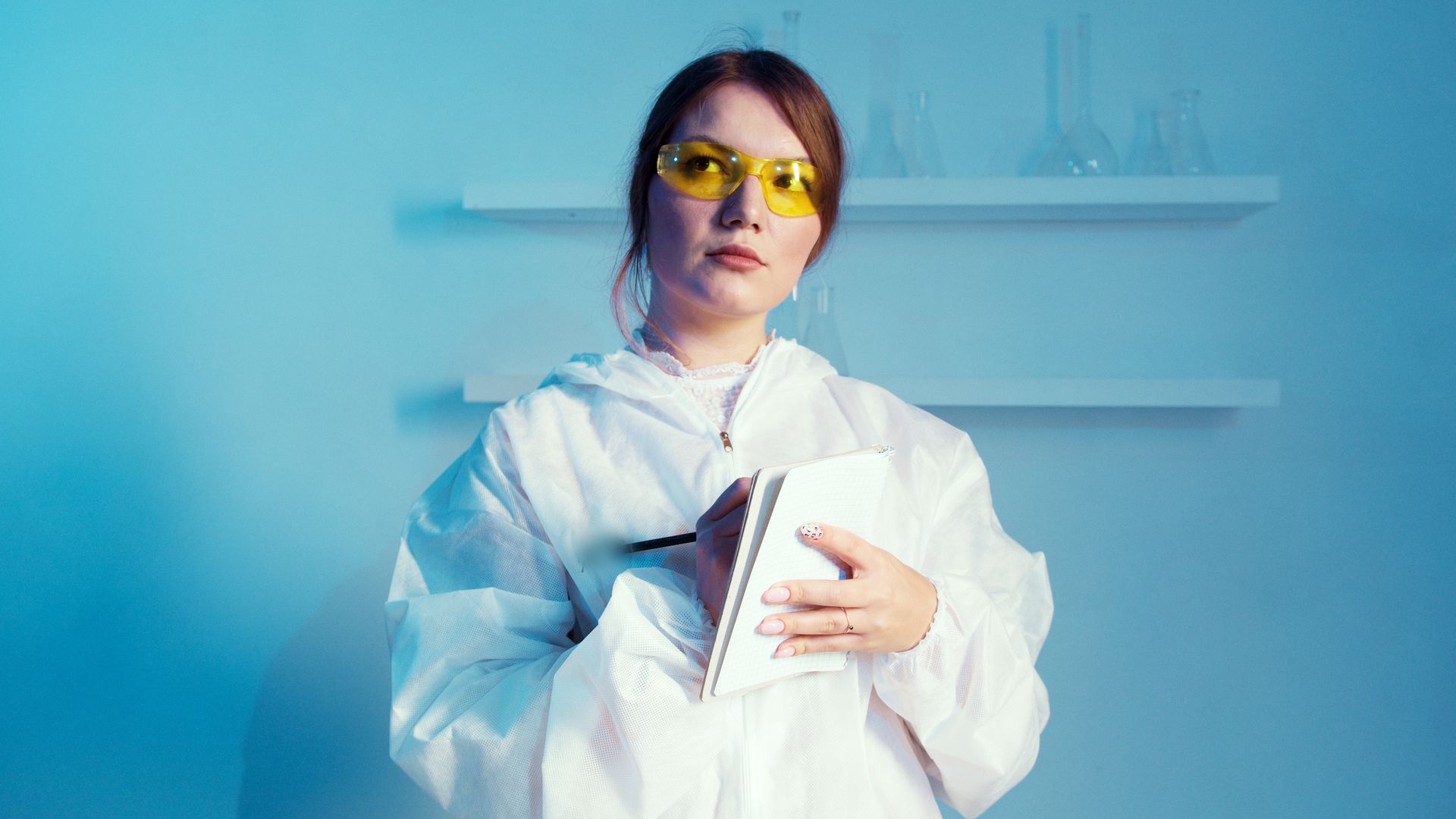 A Woman Wearing Lab Coat While Holding a Notebook