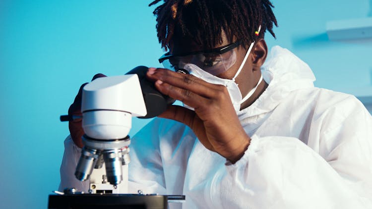 A Man Looking At The Camera While Holding The Eyepiece Of The Microscope