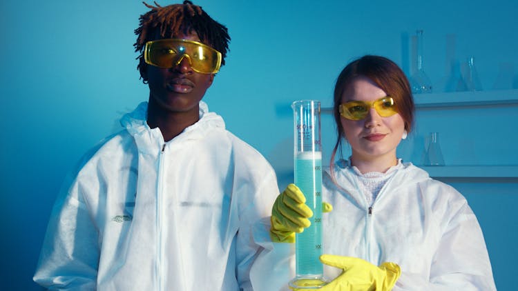 A Man And A Woman Looking At The Camera While Holding A Big Graduated Cylinder