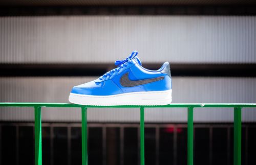 Free Blue Nike sneaker displayed on a green metal railing in an urban setting. Stock Photo