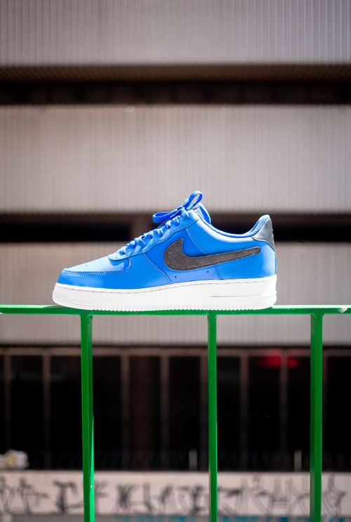 Free Bright blue sneaker with iconic swoosh on a green railing in an urban setting, showcasing modern style. Stock Photo