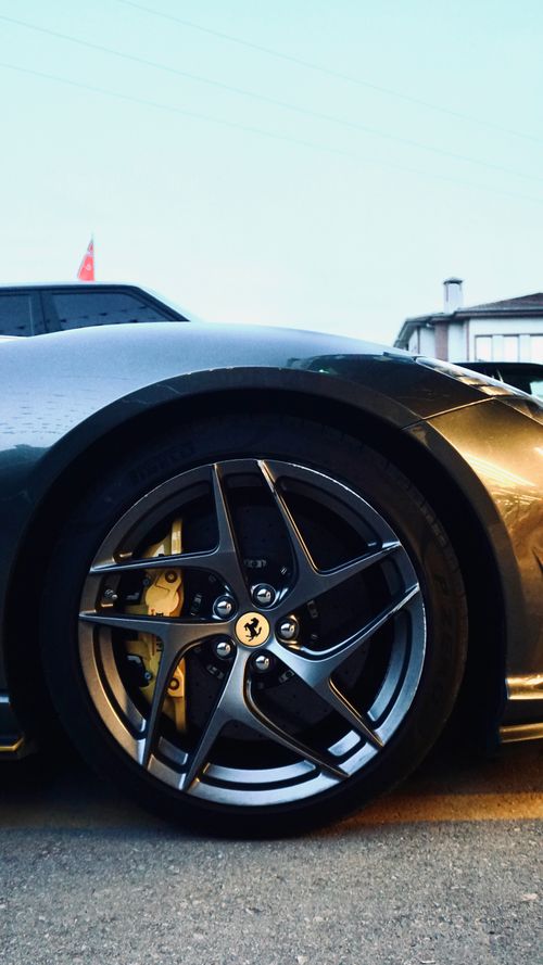 Free Close-up of a gray luxury sports car parked outside with polished alloy wheels at sunset. Stock Photo