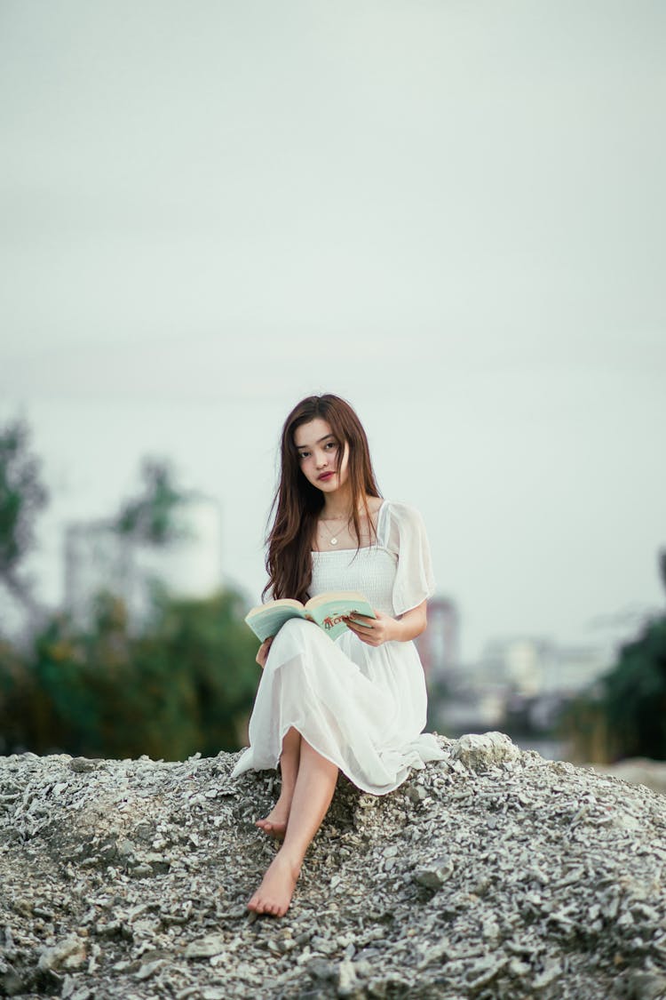 Feminine Barefoot Ethnic Woman With Book Resting On Dry Hill