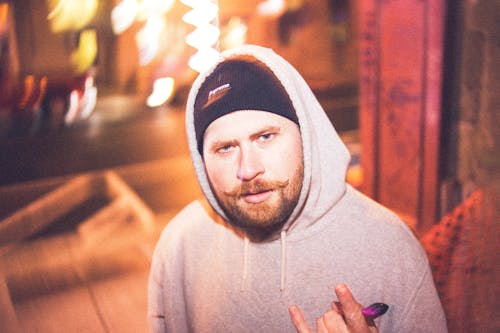 Bearded man in hoodie showing rock gesture on shiny street