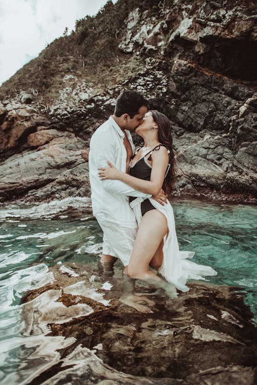 Romantic young couple kissing in sea water near rocky cliff