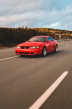 Modern luxury red auto driving fast along roadway with marking lines against green forest