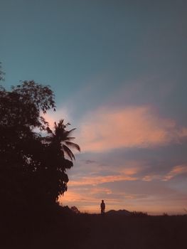 A tranquil scene featuring a person silhouette under a moody tropical sunset sky.
